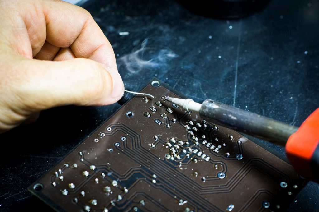 person-soldering-chip-2628105 Hand soldering on a printed circuit board, showcasing electronic craftsmanship.